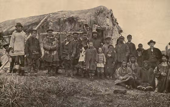orang Chukchi — The photo shows men, women, and children in a mixture of native, Russian, and western dress lined up for a photo in front of a building.