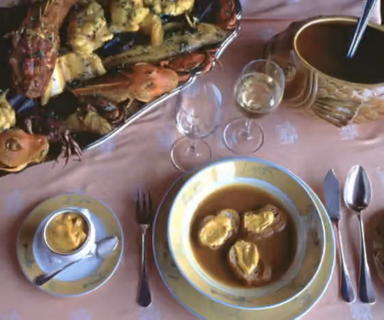 Bouillabaisse — A dish of bouillabaisse with toast spread with rouille sauce, accompanied by white wine and a selection of fish that are typically eaten afterwards.