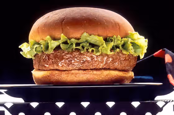 hamburger — A hamburger with a rim of lettuce sitting on a black plate against a black background with a black and red napkin on a black and white-dotted tablecloth.