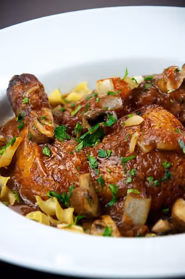 cacciatore — Chicken cacciatore , made with mushrooms, onions, and tomatoes, garnished with parsley, and served over pasta noodles.