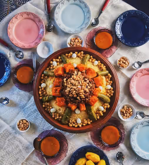 Hidangan Maroko — An overhead view of a communal platter of homemade Moroccan cuscus (كسكس), with chunks of squash (a species similar to kabocha cultivated in Morocco), zucchini halves, chickpeas, and partridge eggs laid on a bed of steamed cuscus, oriented…