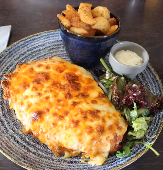 Parmo — Deep-fried chicken parmo (breaded chicken escalope topped with bechamel sauce and cheese) on a plate with chips and garlic sauce