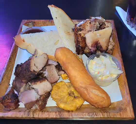 Jamaican cuisine — Jerked pork and chicken served with hard dough bread, jerk sauce, festival, fried pressed plantain and coleslaw at Tracks & Records, Kgn, Jamaica.