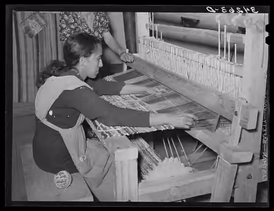 Rug making — B&W photograph of a woman sitting at a machine.