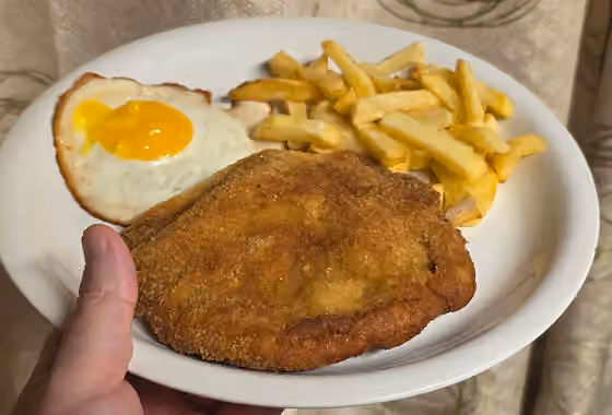 Milanesa — Plato típico de la cocina argentina que incluye una milanesa de carne empanada y frita, acompañada con huevo frito y papas fritas.